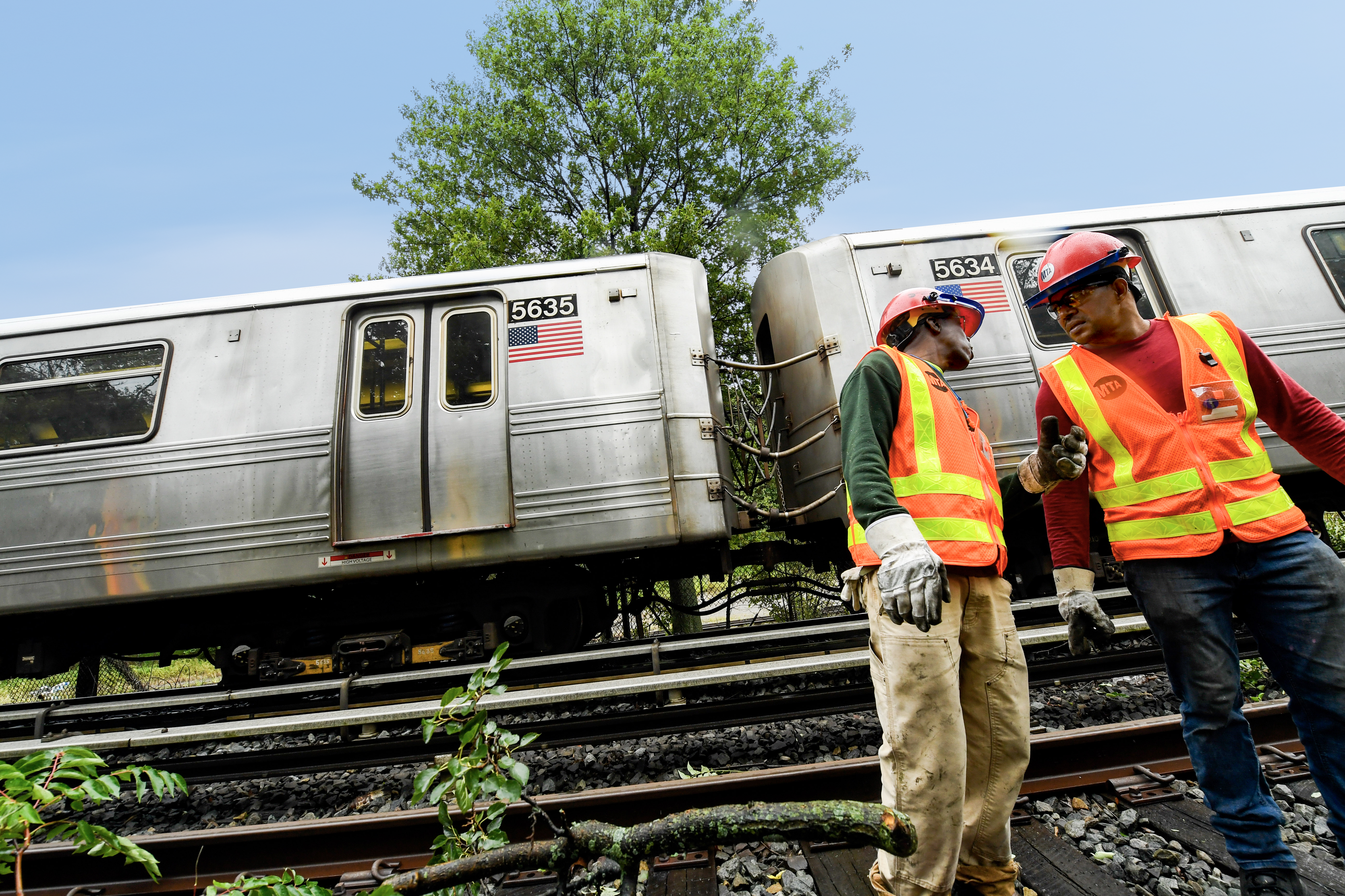 Subway workers alongside a train on elevated tracks obstructed by branches after a storm