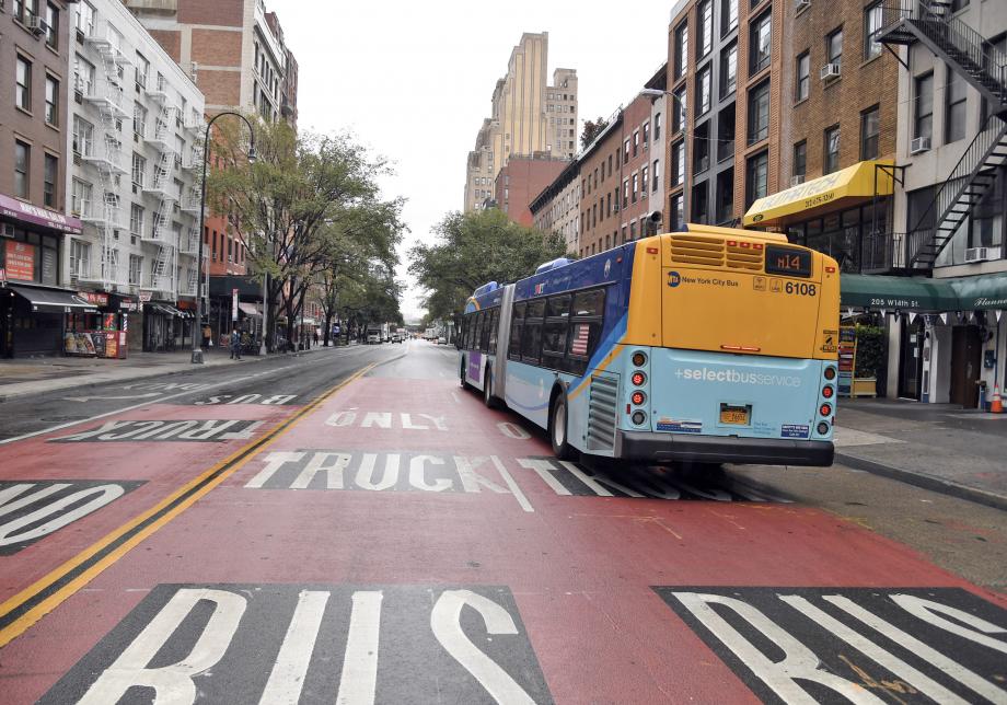 A blue and yellow Select Bus Service bus travels on the traffic-free 14th Street busway. The lanes are clearly marked for buses and trucks only.