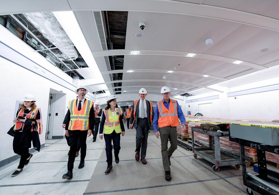 A group of people walk through a train tunnel that is under construction. The group includes Gov. Kathy Hochul, who is wearing a hard hat and a safety vest. 