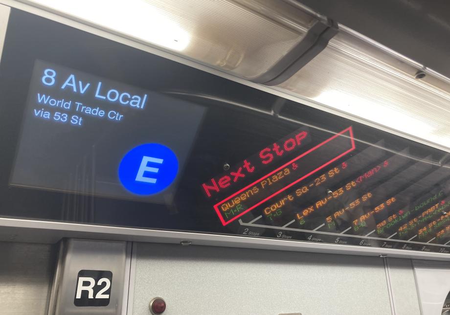 A digital strip map on the E train shows Queens Plaza as the next stop